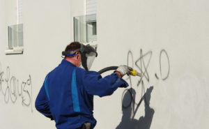 Mann entfernt Graffiti von Hauswand.